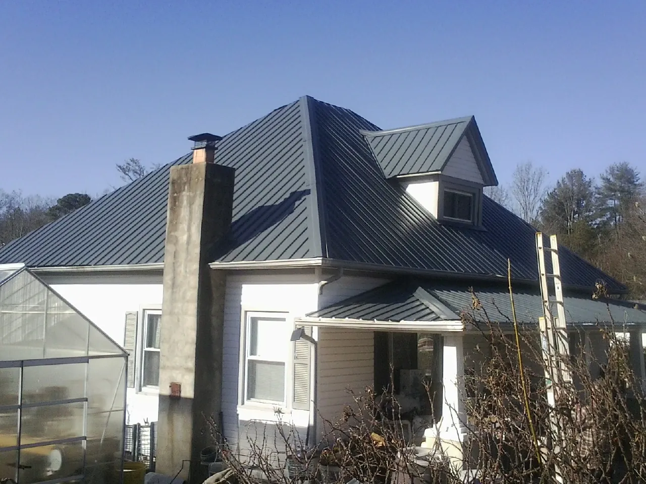 Dark blue standing seam metal roof on a white farmhouse with dormer — Slate & Tile Roof Repair by Roofing Brothers in Anamoose