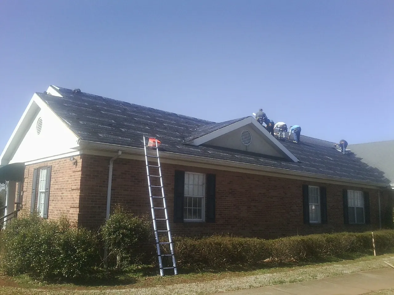 Crew tearing shingles off a brick ranch roof with a ladder set — Emergency Roof Repair work by our crew in Anamoose