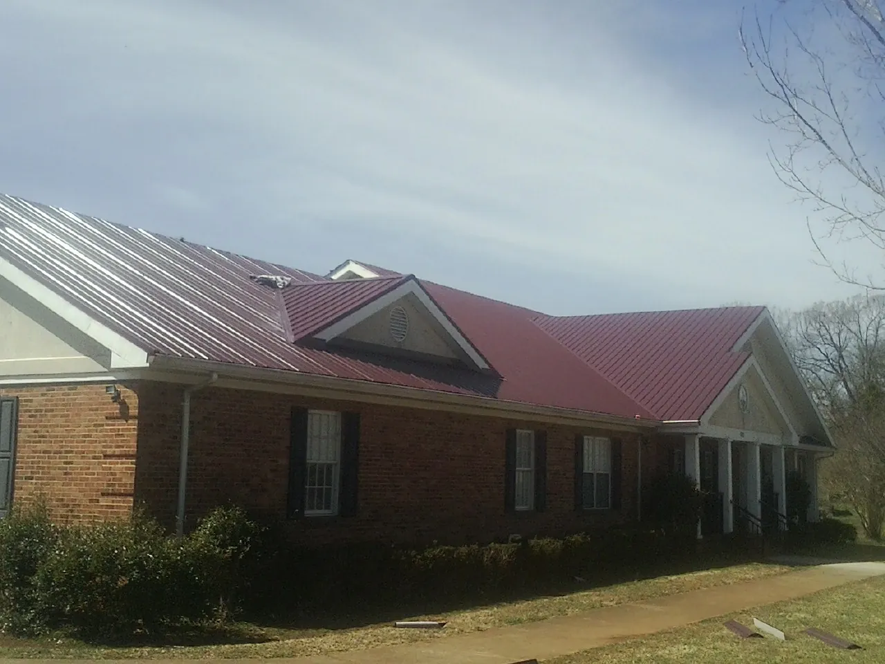 Red metal roof with gabled entries on a long brick building, from a Hail Damage Roof Repair job in Anamoose