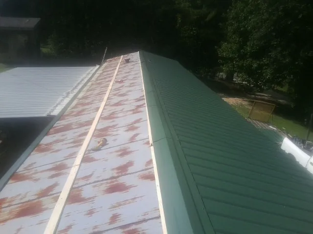 Old rusted panels beside newly installed green metal roofing — Wind Damage Roof Repair by Roofing Brothers in Anamoose