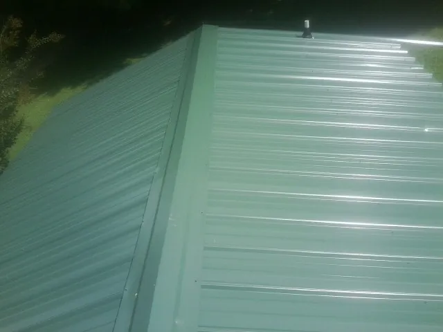 New green metal panels meeting at the ridge of a roof — Flat Roof Repair work by our crew in Anamoose