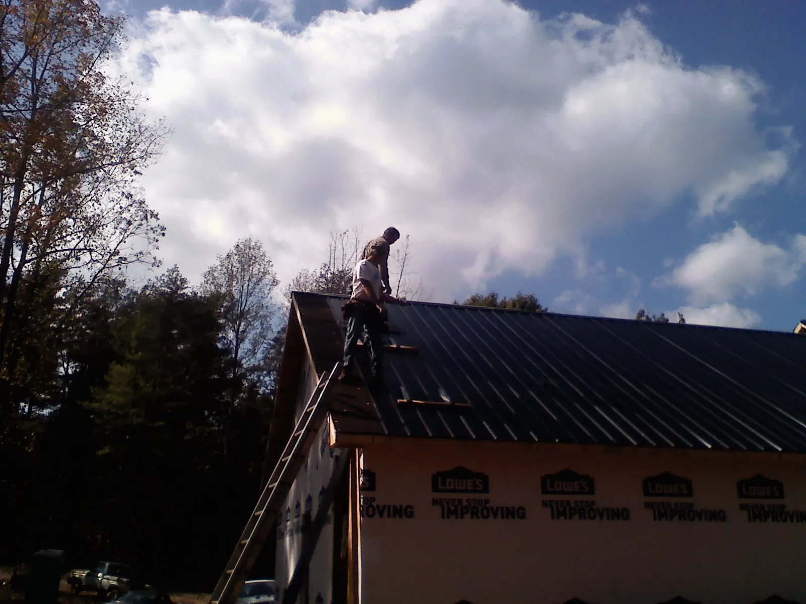 Roofer fastening dark metal panels high against a cloudy sky, from a Roof Inspection job in Anamoose