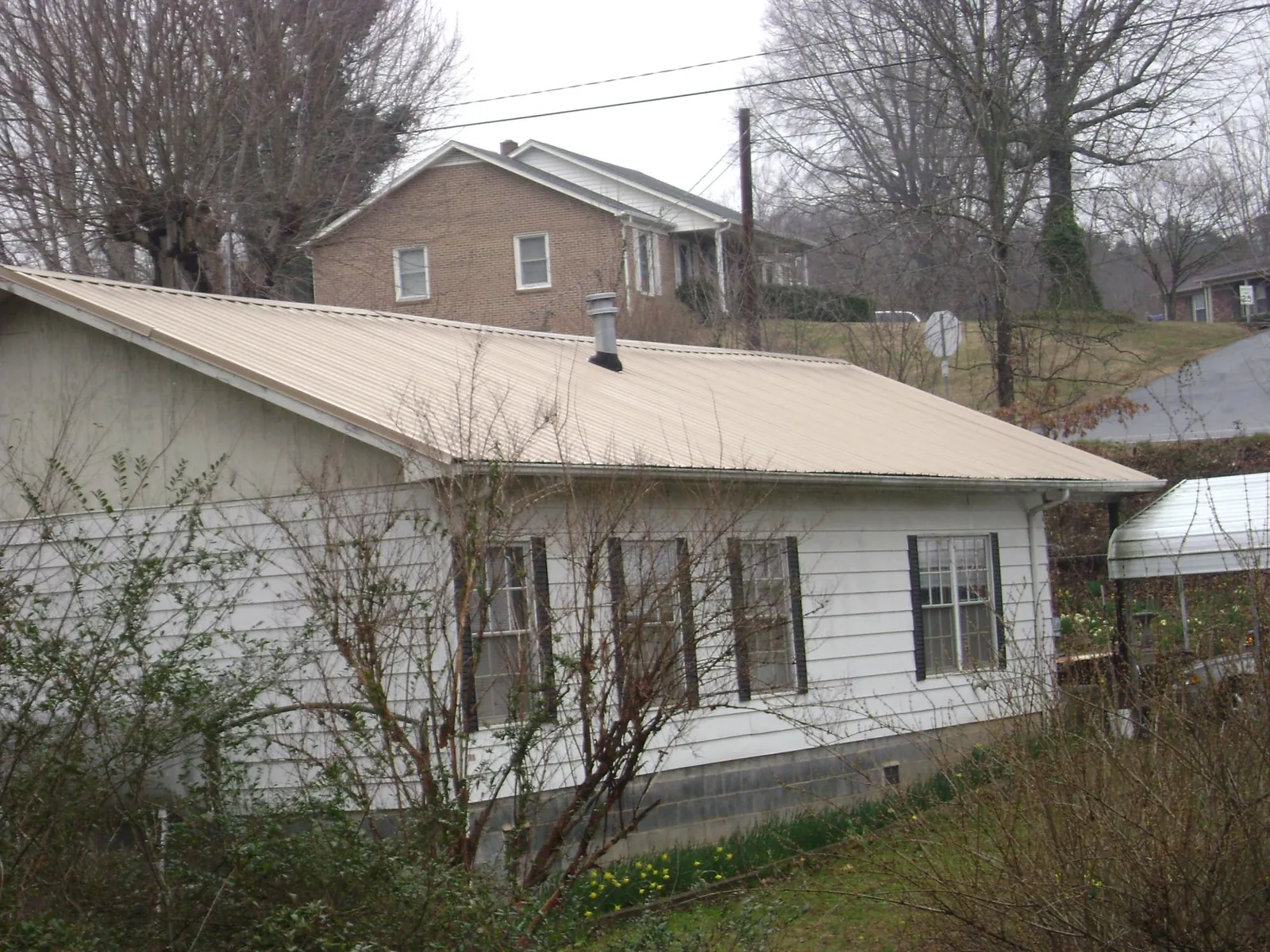 Tan metal roof on a white sided house set into a hillside — Commercial Roofing by Roofing Brothers in Anamoose