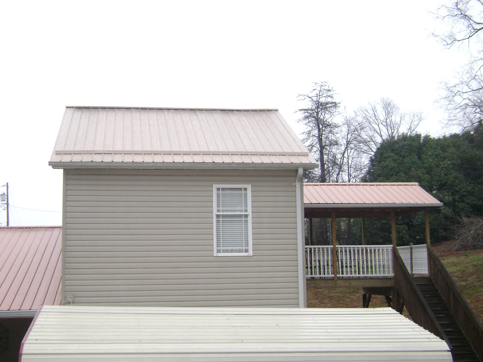 Tan metal roofs on a two story addition and attached porch, from a Roof Replacement job in Anamoose